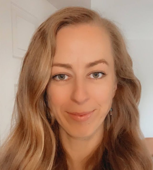 Headshot of Jessica Taylor with long, wavy, blonde hair, wearing a dark-coloured top, against a light-coloured background.